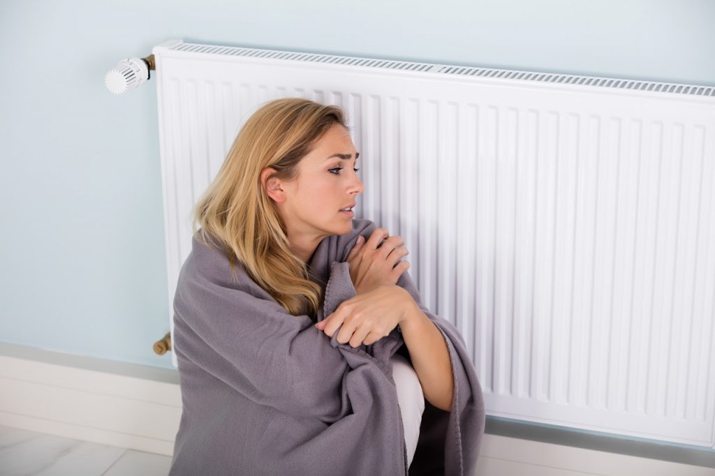 woman with a blanket sitting near a thermostat
