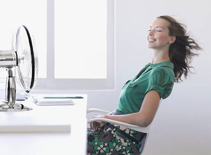 A Woman Sitting on the Chair in Front of Table Fan and Her Hairs Are Blowing