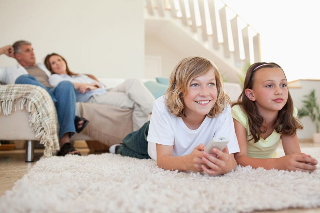 Siblings Lying on the Carpet Watching Tv and Their Parents Sitting on Sofa Watching Them Happily
