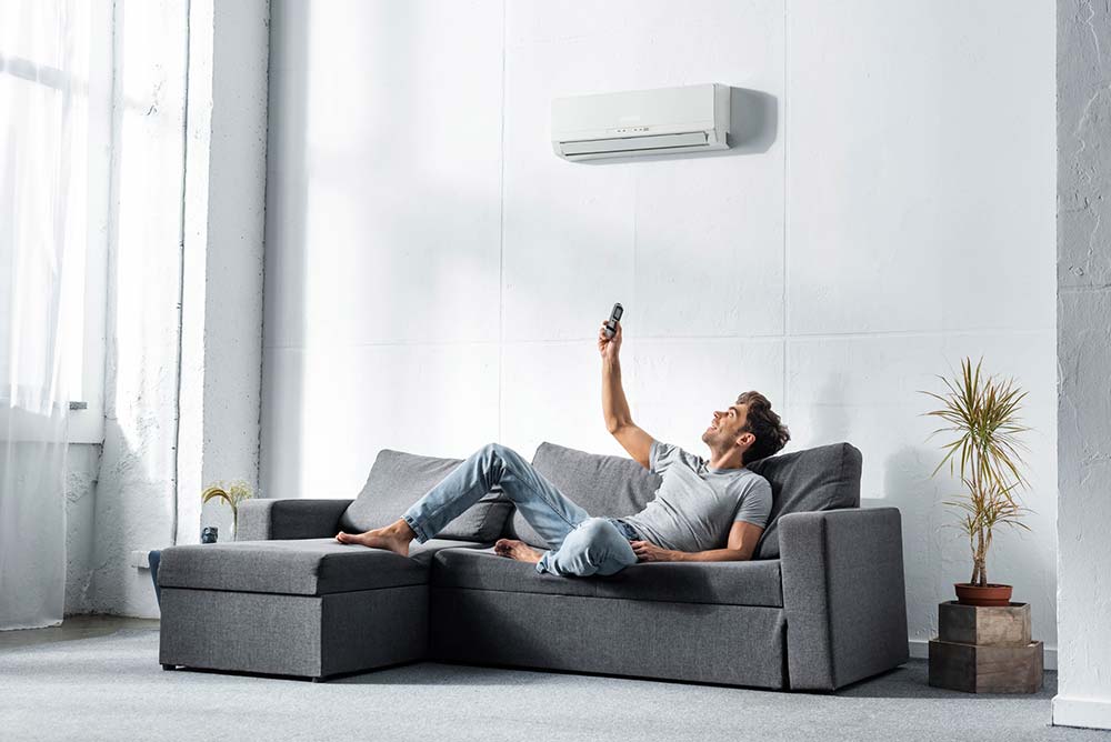 Man Lying on Sofa and Switching on Air Conditioner