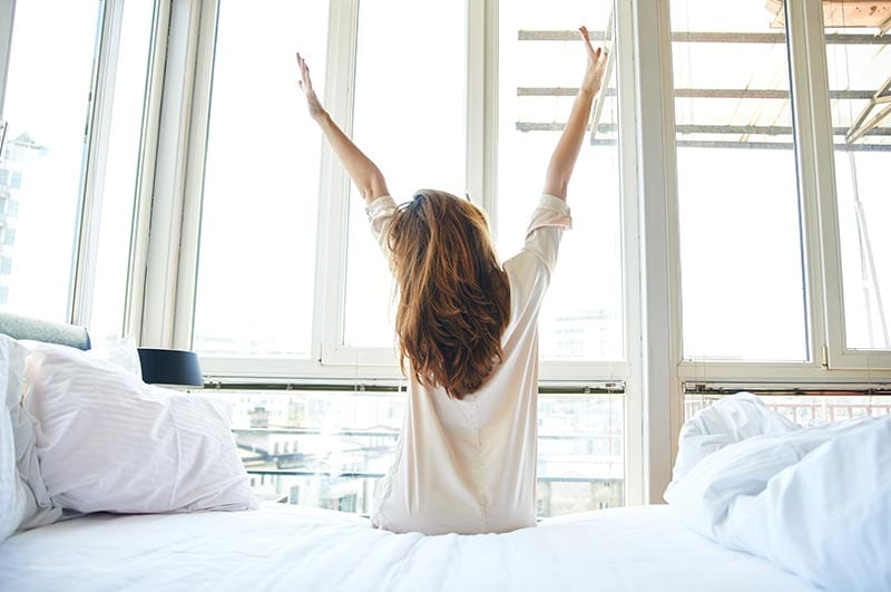 Woman Sitting on the Bed and Hand up Wake up on Morning in Simple White Room With Air Condition